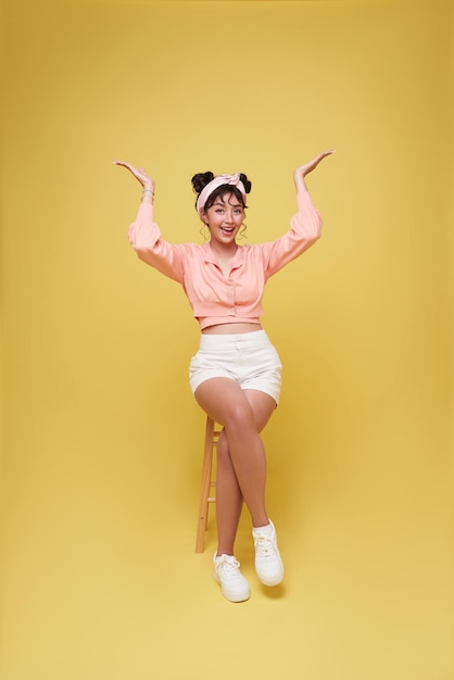 Free Photo beautiful asian teen girl sitting on chair and relax hand up isolated on yellow background