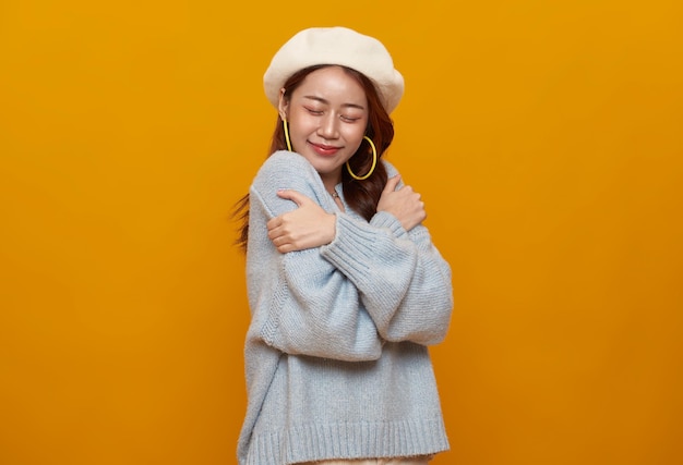 Free photo beautiful asian teenager woman hugging and embracing herself isolated on studio yellow background