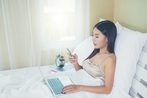 Free photo a beautiful asian woman relaxes and works with a laptop computer, reading at home.