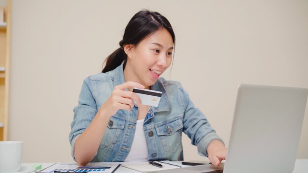 Free photo beautiful asian woman using laptop buying online shopping by credit card while wear casual sitting on desk in living room at home.