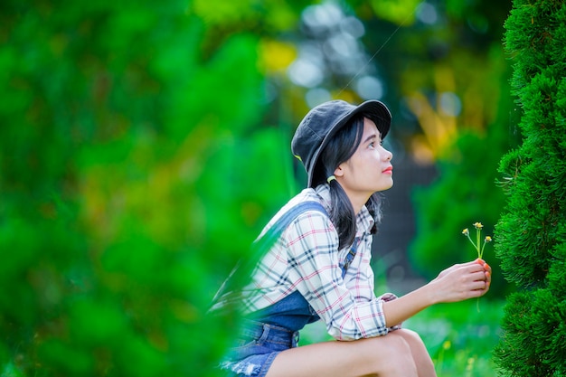 Free photo a beautiful asian woman wearing a hat to relax and enjoy in the green garden as a backdrop.