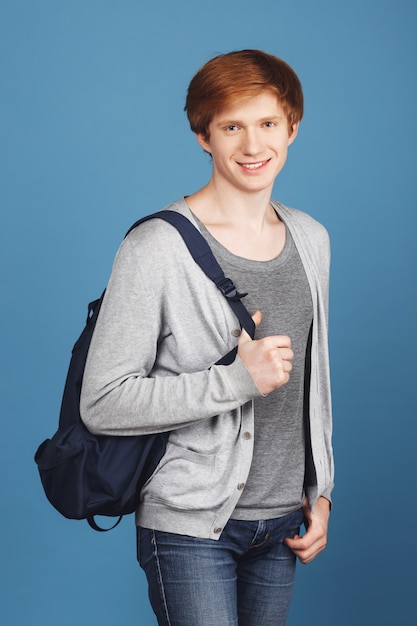 Free Photo beautiful good-looking cheerful student with ginger hair in casual outfit smiling, holding backpack and hand in pocket,  with relaxed and happy expression.