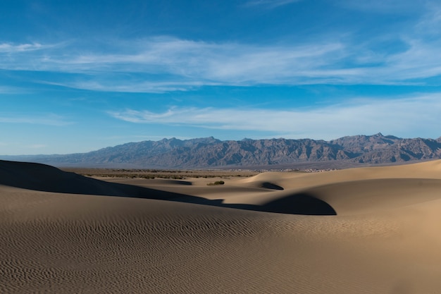 Free photo beautiful shot of a desert with trails on the sand and rocky hills under the calm sky