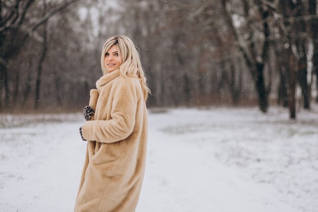 Free photo beautiful woman in winter coat walking in park full of snow