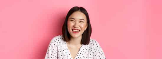 Free photo beauty and lifestyle concept closeup of happy asian woman laughing and having fun standing over pink