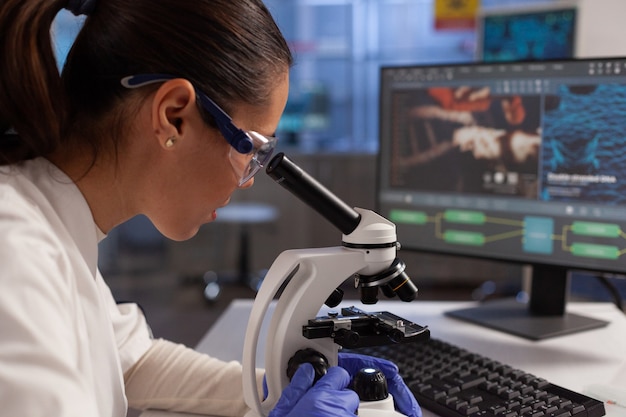 Free photo biochemist working on microscope for cell illustration on computer screen in chemical laboratory. scientist woman analyzing virus dna, cell tissue, diagram of plasma and hemoglobin nucleus