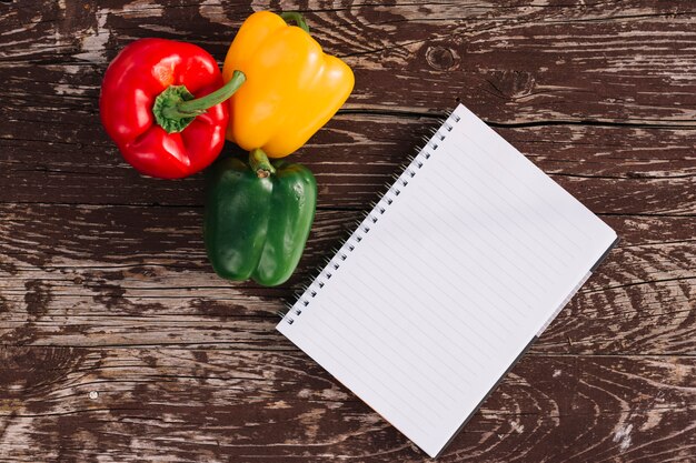 Blank single line spiral notepad with red; yellow and green bell peppers on wooden texture backdrop