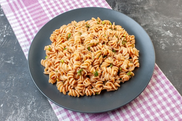 Foto gratuita pasta rotini vista dal basso su piatto rotondo su tovaglia a quadretti bianca rosa su superficie scura