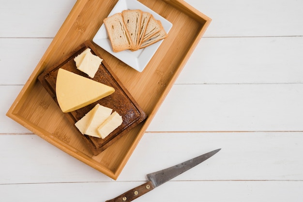 Free photo bread slices and cheese wedges on wooden tray with knife