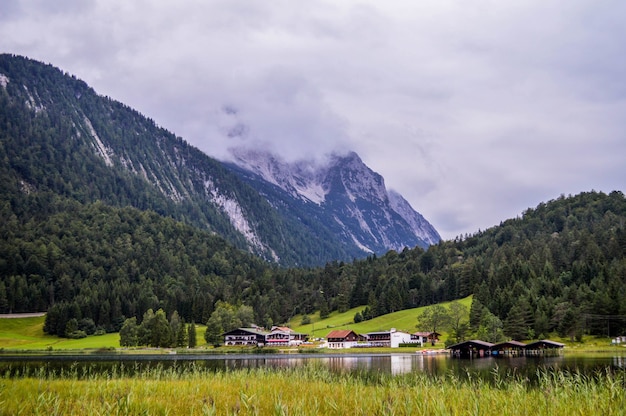 Foto gratuita vista mozzafiato sul fiume tra gli alberi verdi e la montagna innevata sotto un cielo nuvoloso