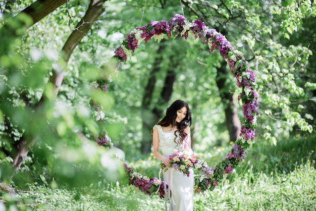 Foto gratuita la sposa con lunghi capelli scuri si siede su un grande cerchio di lillà