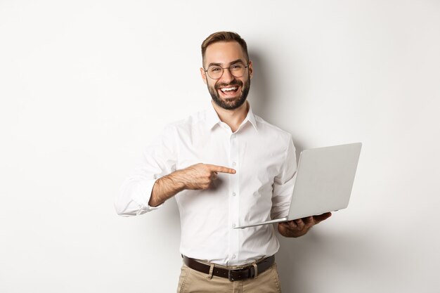 Business. Handsome manager in glasses working on laptop, pointing at computer and smiling pleased, standing  