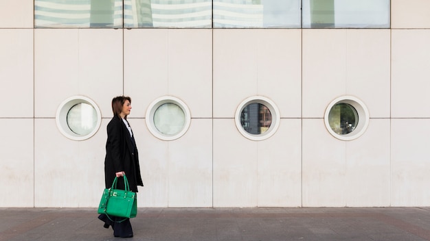 Foto gratuita donna di affari che cammina in strada con la borsa verde