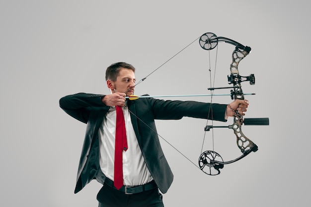 Free photo businessman aiming at target with bow and arrow, isolated on gray background.