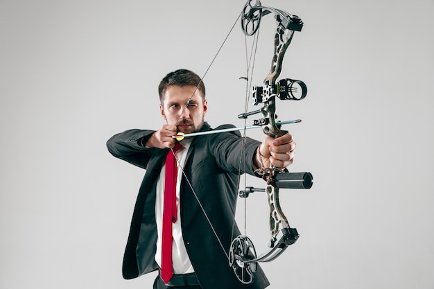 Free photo businessman aiming at target with bow and arrow isolated on gray  background.