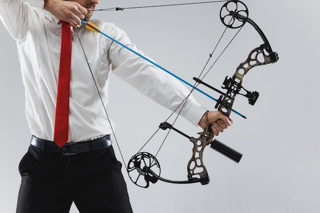 Free photo businessman aiming at target with bow and arrow, isolated on gray studio background. the business, goal, challenge, competition, achievement concept