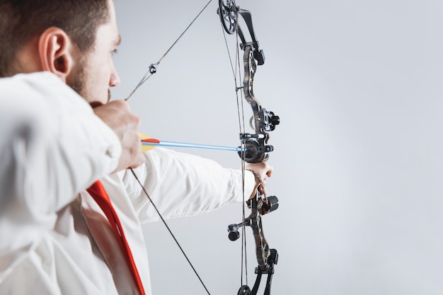 Free photo businessman aiming at target with bow and arrow, isolated on gray studio background.