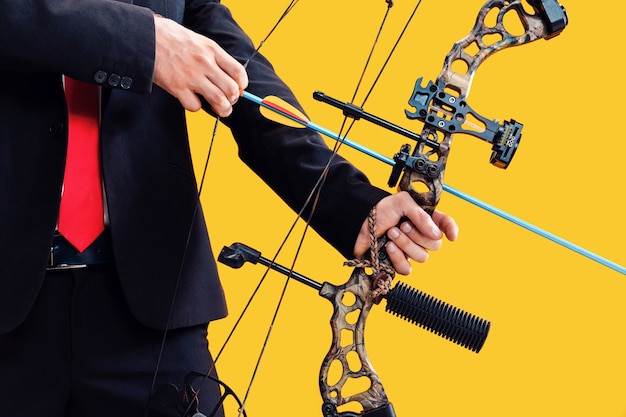 Free photo businessman aiming at target with bow and arrow, isolated on yellow studio background. the business, goal, challenge, competition, achievement concept