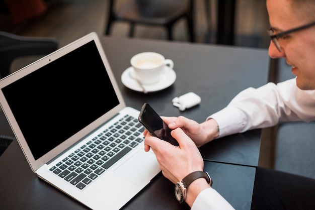 Free Photo a businessman using the mobile phone in front of laptop with coffee cup on table