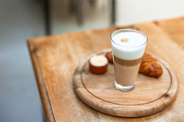 Foto gratuita cappuccino in vetro con croissant su vassoio circolare in legno