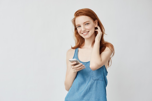 Free photo cheerful sincere foxy girl with freckles smiling holding phone.