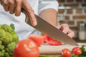 Free photo chef's male hand cutting the tomato with sharp knife on board