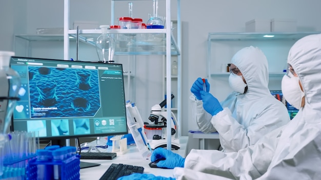 Free photo chemist doctor in ppe suit working at pc while lab technician using microscope. team of scientists examining vaccine evolution with high tech for researching treatment against covid19 virus