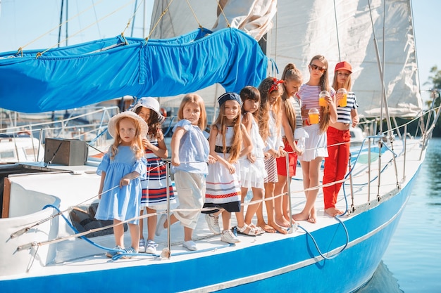 Foto gratuita i bambini a bordo dello yacht del mare bevono succo d'arancia. le ragazze adolescenti o bambini contro il cielo blu all'aperto. vestiti colorati. concetti di moda per bambini, estate soleggiata, fiume e vacanze.