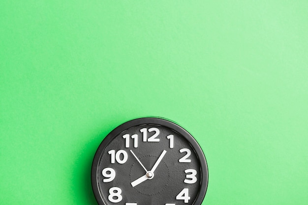 Circular black clock on green wall backdrop