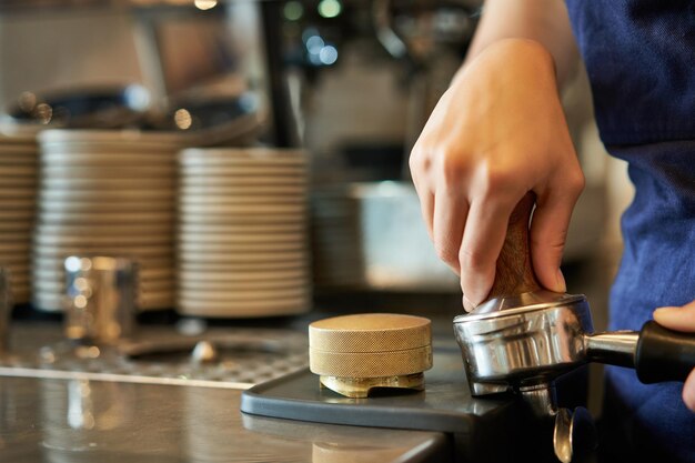 Free photo close up of barista female hands pressing coffee into tamper prepares order in cafe behind counter