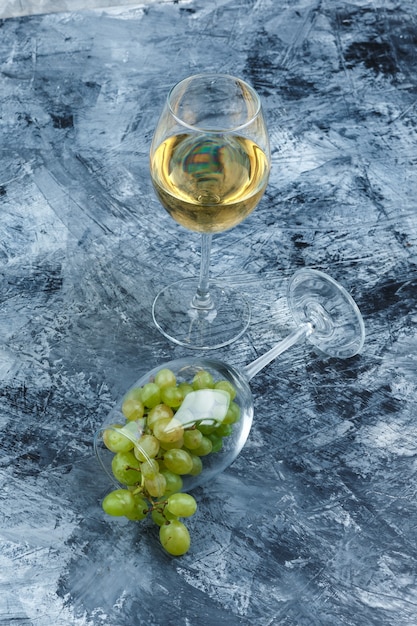 Free photo close-up glass of white grapes with glass of whisky on dark blue marble background. vertical