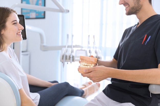 Free photo close-up of a male dentist showing teeth model to patient