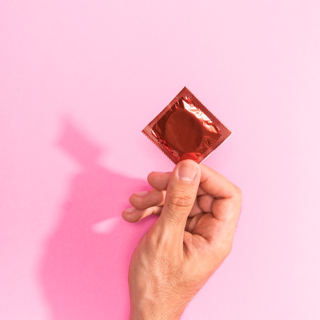 Free photo close-up man holding up a red condom