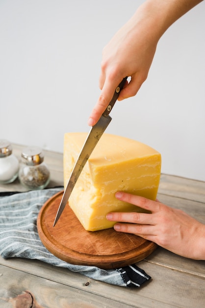 Free photo close-up of a person cutting the cheese with knife on round chopping board