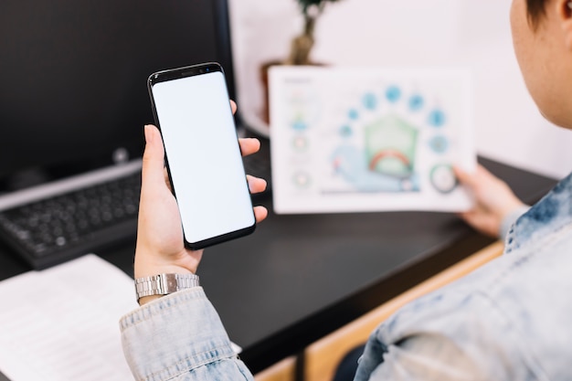 Free photo close-up of a person holding cellphone with blank screen at workplace