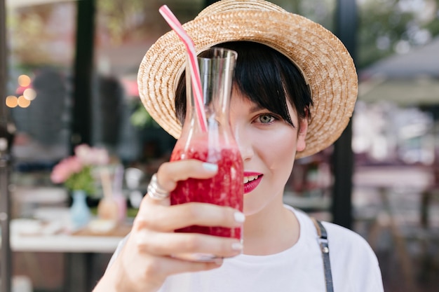 Foto gratuita ritratto del primo piano di giovane donna elegante con capelli corti neri e pelle pallida che tiene un bicchiere di limonata ghiacciata