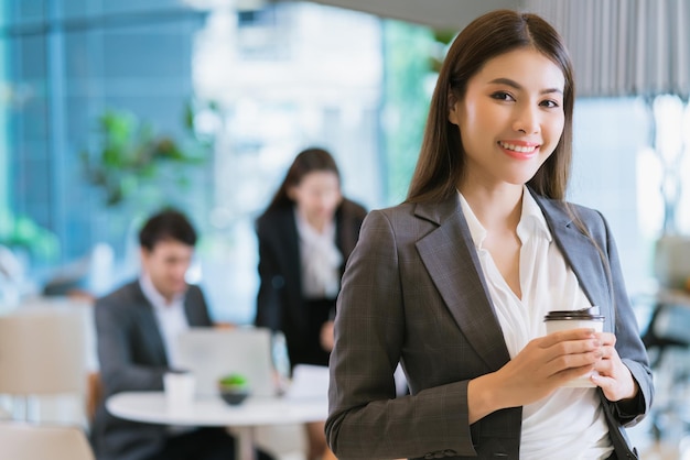 Free photo close up smart attractive asian business female smile hand hold hot drink with modern office background