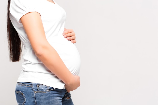 Free photo close-up of unrecognizable pregnant woman with hands over tummy at white wall