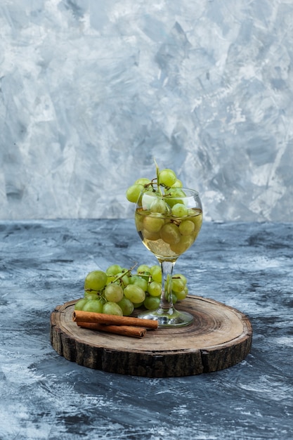 Free photo close-up white grapes, cinnamon, glass of whisky on wooden board on dark blue marble background. vertical