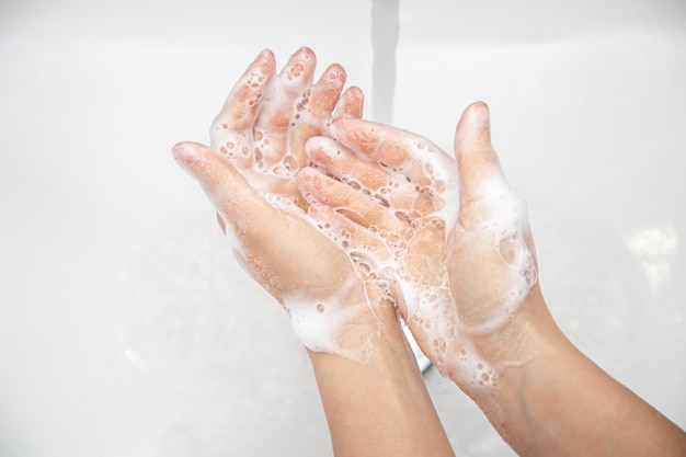 Free photo close up a woman is washing soap foam from her hands under running water.