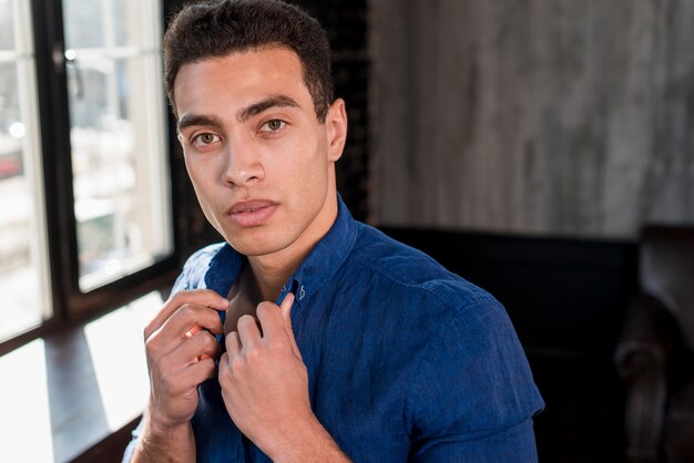 Free photo close-up of a young man holding a shirt collar with his hand looking at camera