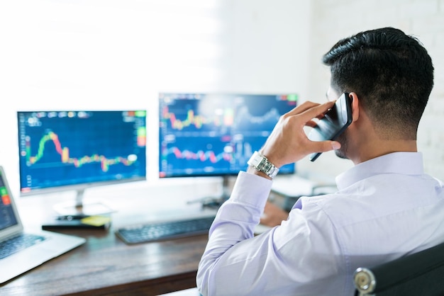 Free photo closeup of freelance finance professional discussing with client through mobile phone while trading stocks at home