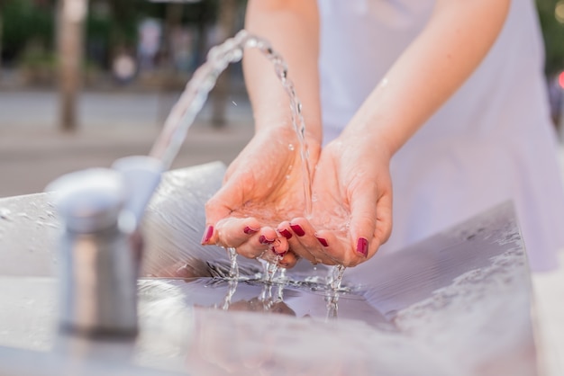 Free photo closeup on woman hand catching water. splashing drops on sunny summer outdoors background. environment and health concept. flowing fountain cool drink