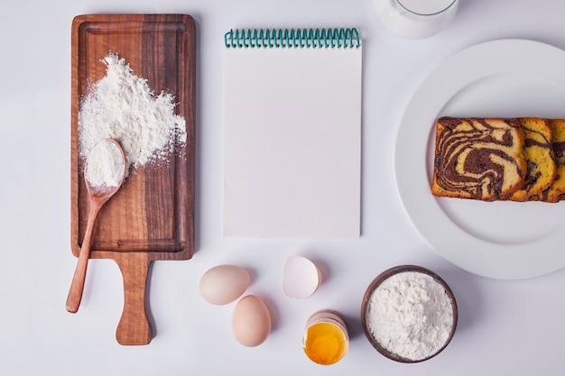 Free Photo cocoa pie sliced and served in a white ceramic plate with ingredients and a receipt book around.