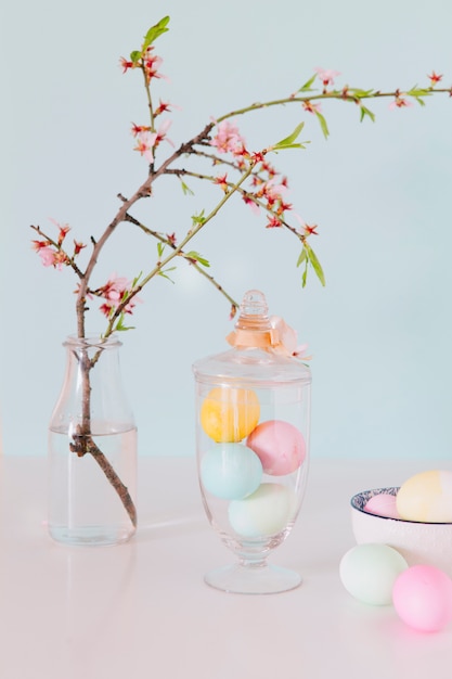 Free Photo colourful easter eggs near flower twig in vase with water and bowl