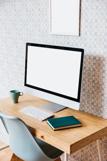 Free Photo computer with blank white screen and diary over wooden desk