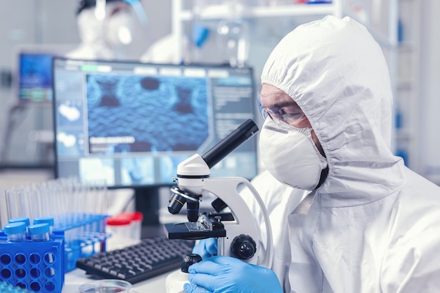 Free Photo concentrated scientist in ppe equipment looking into the microscope in laboratory. scientist in protective suit sitting at workplace using modern medical technology during global epidemic.