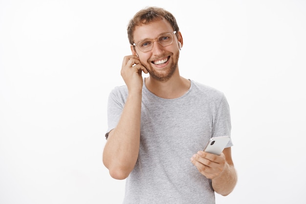 Free photo confident and pleasant european man signing expensive deals on go talking with clients in wireless earphones holding smartphone and smiling friendly and joyful having nice calm conversation