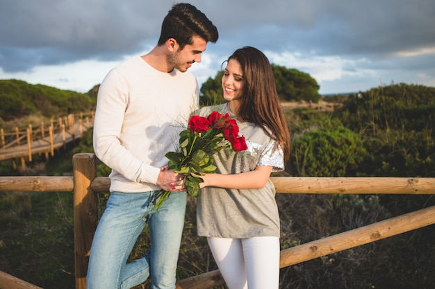 Free photo couple leaning on a railing of a bridge with a bouquet of roses