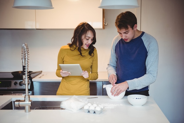 Free photo couple using digital tablet while preparing cookies in kitchen